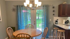 A dining area with a round table and six wooden chairs, a chandelier, and a kitchen counter with stools.