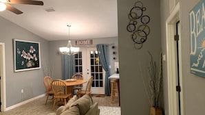A living room with a sofa, dining table, and chairs. There is a 'HOME' sign above the door.