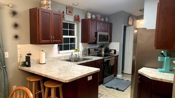 A kitchen with dark wooden cabinets, a granite countertop, a built-in microwave, and a stainless steel refrigerator.