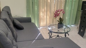 Un canapé d’angle gris, une table basse en verre et une orchidée en pot.