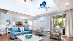 Ein geräumiges Wohnzimmer mit einem blauen Sofa, gemusterten Sesseln, einem Couchtisch mit Glasplatte und einem Wandgemälde mit Fischmotiven.