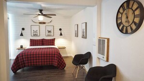 A bedroom with a bed, a ceiling fan, a clock, and framed pictures on the wall.