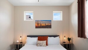 Un dormitorio ordenado con una cama grande, dos mesitas de noche con lámparas y dos cuadros enmarcados en la pared.