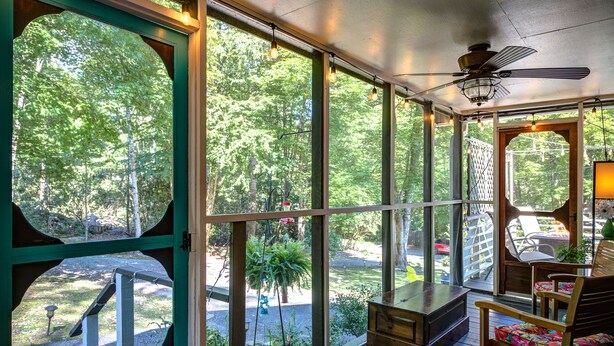 A covered porch with large windows, a ceiling fan, and wooden furniture. - New! Cottage On The Rocks, Pet Friendly, Hot Tub, Central Location (Banner Elk)