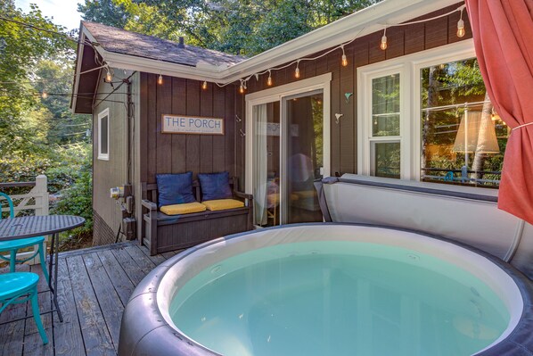 Een houten terras met een jacuzzi, een veranda met een bord waarop “THE PORCH” staat, en een tafel met stoelen.