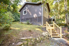 A wooden cabin with a wooden staircase leading to a deck, surrounded by dense forest. - New! Cottage On The Rocks, Pet Friendly, Hot Tub, Central Location (Banner Elk)