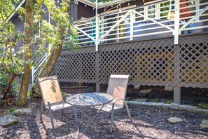 An outdoor seating area with a round table and two chairs, surrounded by a wooden fence and trees. - New! Cottage On The Rocks, Pet Friendly, Hot Tub, Central Location (Banner Elk)