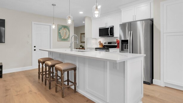 Una cocina moderna con armarios blancos, un refrigerador de acero inoxidable, un microondas y una isla grande con taburetes de bar.