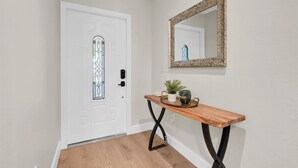 Un pasillo con una puerta blanca, una consola de madera con un espejo y una planta en maceta.