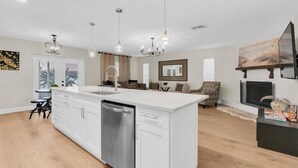 Una cocina moderna con armarios blancos, una isla central con lavamanos e iluminación colgante.