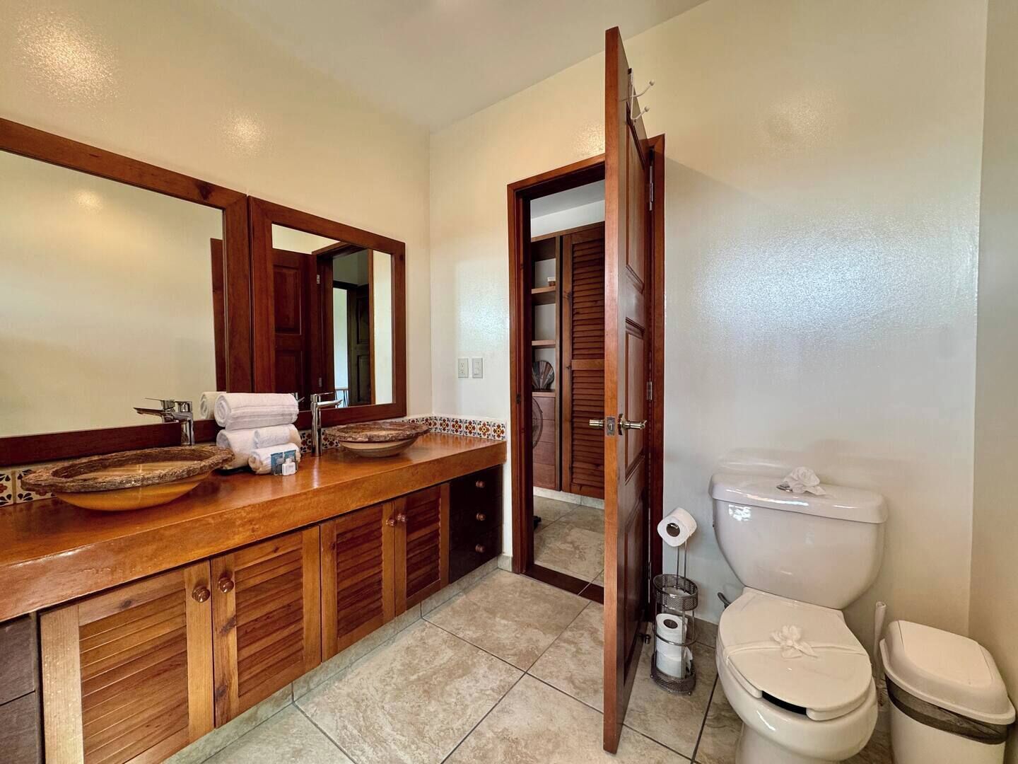 Un baño con tocador de madera, un espejo grande, lavamanos, inodoro y zona de ducha.