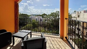 Een balkon met een tafel en stoelen, uitzicht op gebouwen en bomen, en een boog.