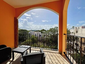 Un balcon avec une table et des chaises, une vue sur des immeubles et des arbres, et une arche.
