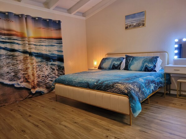A bedroom with a bed, a desk, and a mirror with lights.
