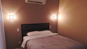 Una cama pequeña y bien arreglada en una habitación con dos luces fijadas a la pared y un equipo de aire acondicionado arriba.
