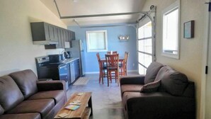 Un espacio habitable compacto con kitchenette, dos sofás de cuero, una mesa de centro de madera y un comedor con sillas.