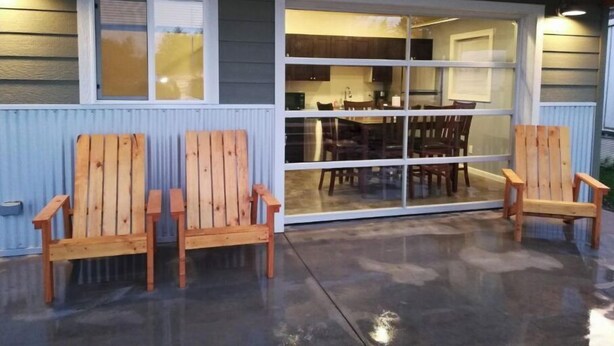 Un patio cubierto con dos sillas Adirondack de madera, piso de concreto y puerta corrediza de vidrio que da a un comedor con mesa y sillas.