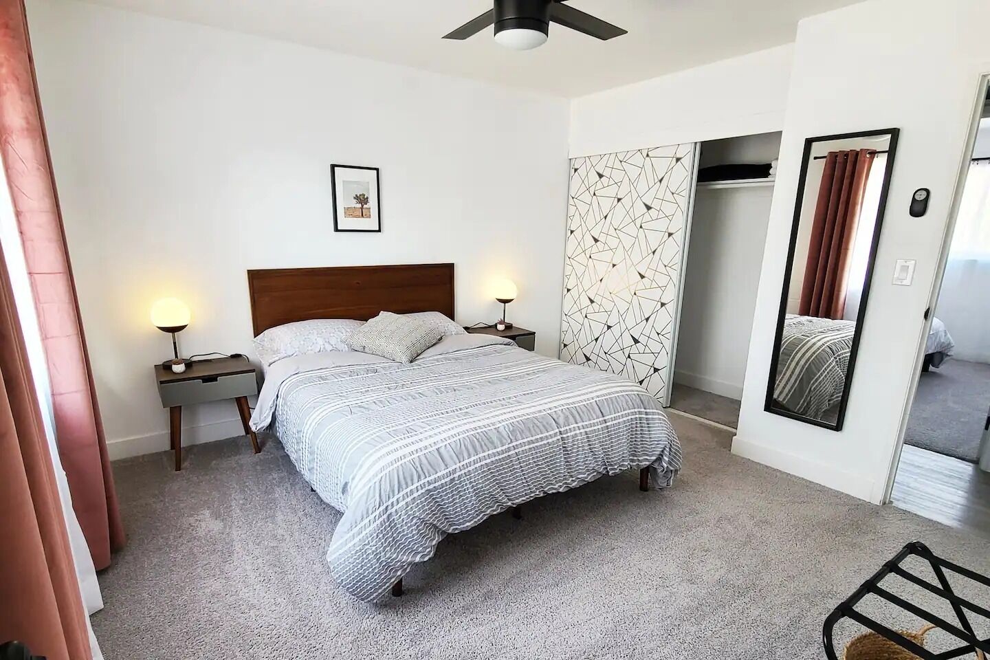 Une chambre à coucher comprenant un lit, des tables de chevet, un miroir fixé au mur et une porte donnant sur une autre pièce.