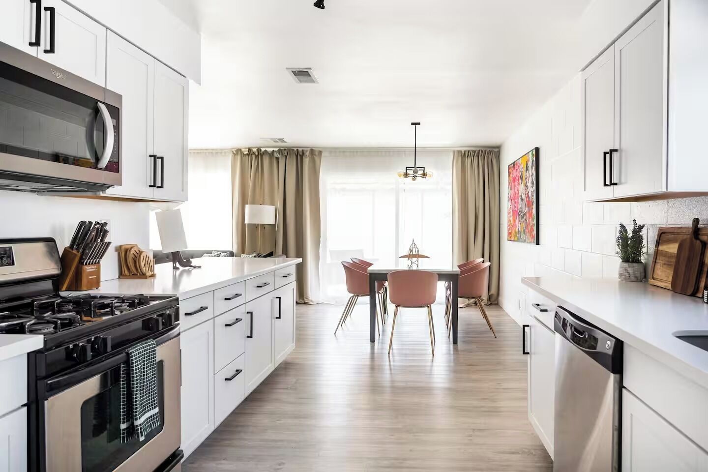 A modern kitchen with white cabinetry, a built-in microwave, a gas stove, and a dining area with a table and chairs.