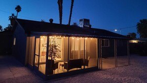 Une maison moderne dotée d’une véranda en verre, d’un patio avec des chaises et de palmiers en arrière-plan.