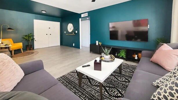 Un salon moderne avec des murs de couleur turquoise, un téléviseur à écran plat, un ventilateur de plafond et un canapé agrémenté d’un tapis à motifs.