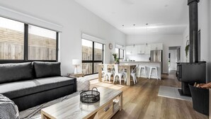 Een moderne woonkamer met een bank, eettafel en keuken, met witte kasten en een zwart fornuis.