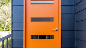 Een fel oranje deur met twee rechthoekige ramen en een metalen handgreep.
