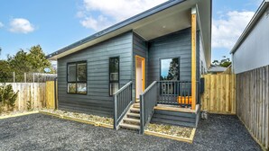 Een modern huis met twee verdiepingen, een donkere gevel, een houten terras en een oprit met grind.
