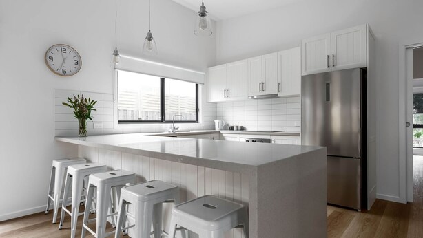 Een moderne keuken met een centraal eiland, witte kastjes en roestvrijstalen apparatuur, en barkrukken.