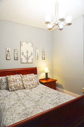 A bedroom with a wooden bed, a nightstand with a lamp, and wall-mounted artwork.