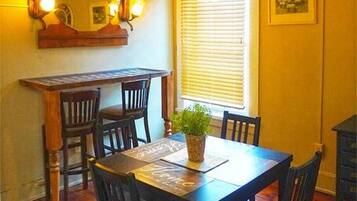 A dining area with a wooden table and chairs, a hanging light fixture, a window with blinds, and a mirror on the wall.