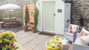 A cozy outdoor seating area with a table and chairs, a small shed with a door, and potted plants.