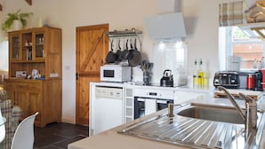 A compact kitchen with a microwave, kettle, and toaster. There's a wooden cabinet with glass doors and a window above the sink.