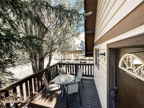 A wooden deck with a glass table and chairs, a dark door with a window, and a tree in the background. - Alpine Adventure Haven- Walk to Village Gondola, Biking &Trails BTC 10013 (Mammoth Lakes)