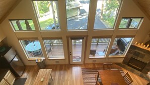A spacious kitchen with a large island, a dining area with a long wooden table, and a view of a backyard through large windows. - Kid Friendly Cabin with Mother-in-law Suite and Hot Tub! (Ronald)