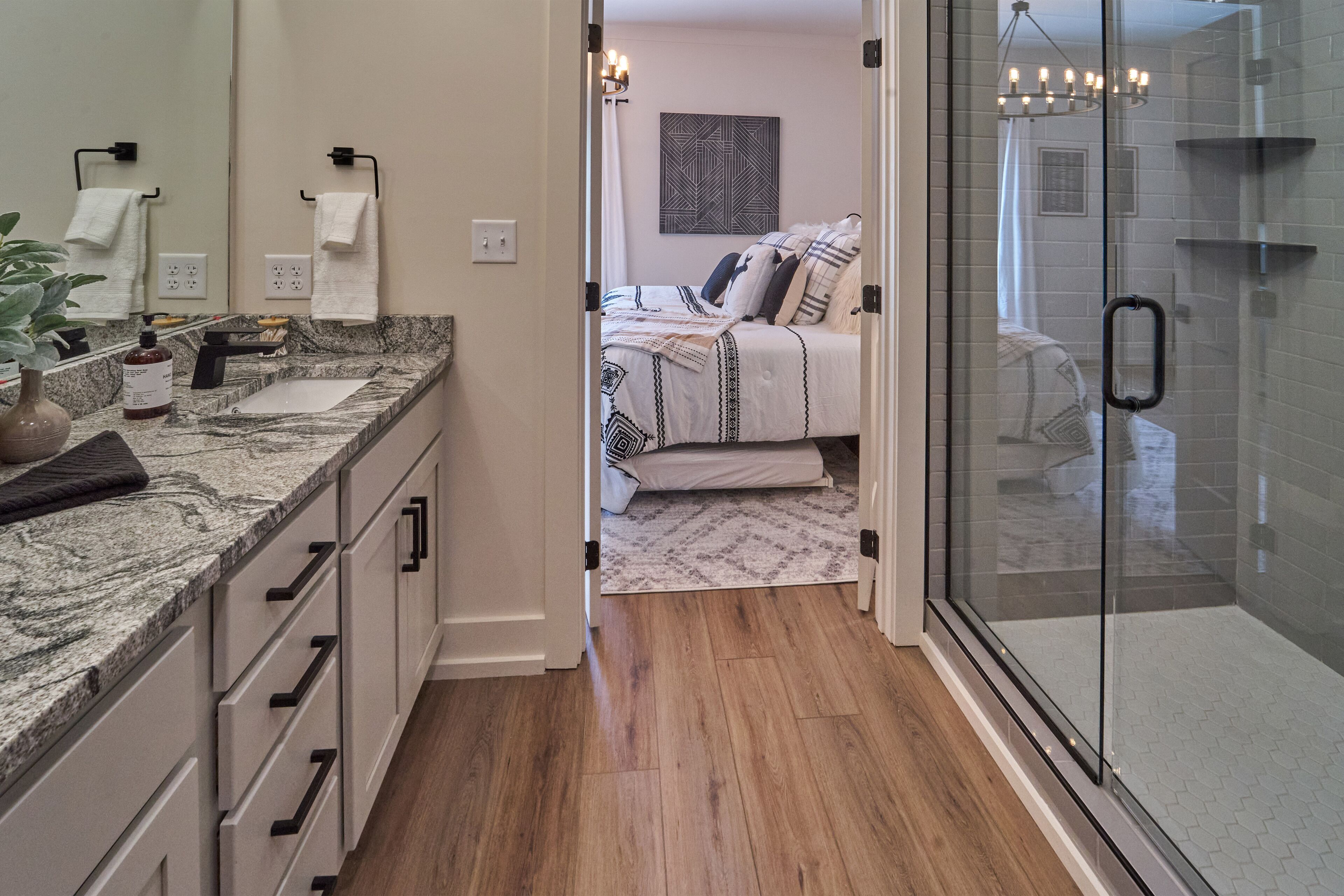 A modern bathroom with a glass shower enclosure, a marble countertop, and a bed with patterned bedding.