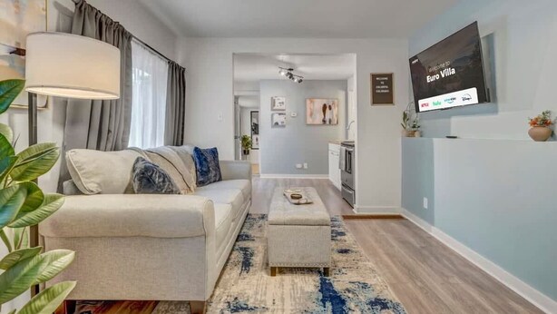 Ein modernes Wohnzimmer mit einer Couch, einem Hocker und einem an der Wand befestigten Fernseher.