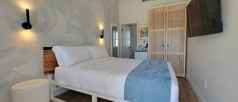A modern bedroom with a bed, wall-mounted lights, a ceiling fan, and a TV.