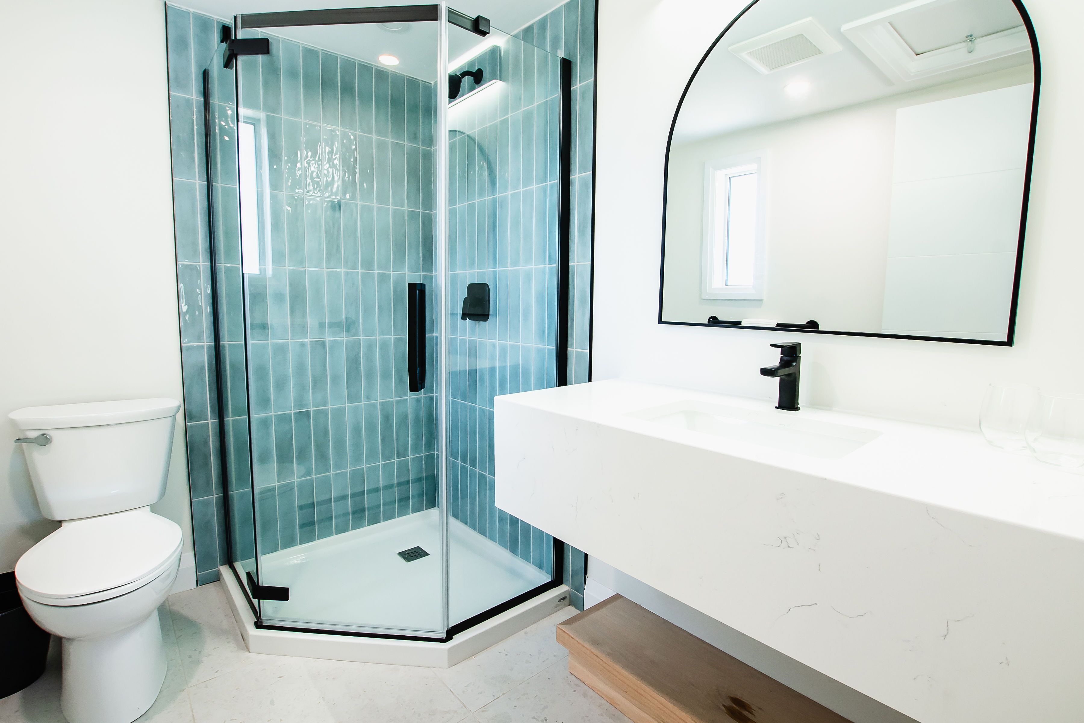 Et moderne badeværelse med et glasafskærmet brusebad, et hvidt toilet og et stort spejl over en hvid vask.