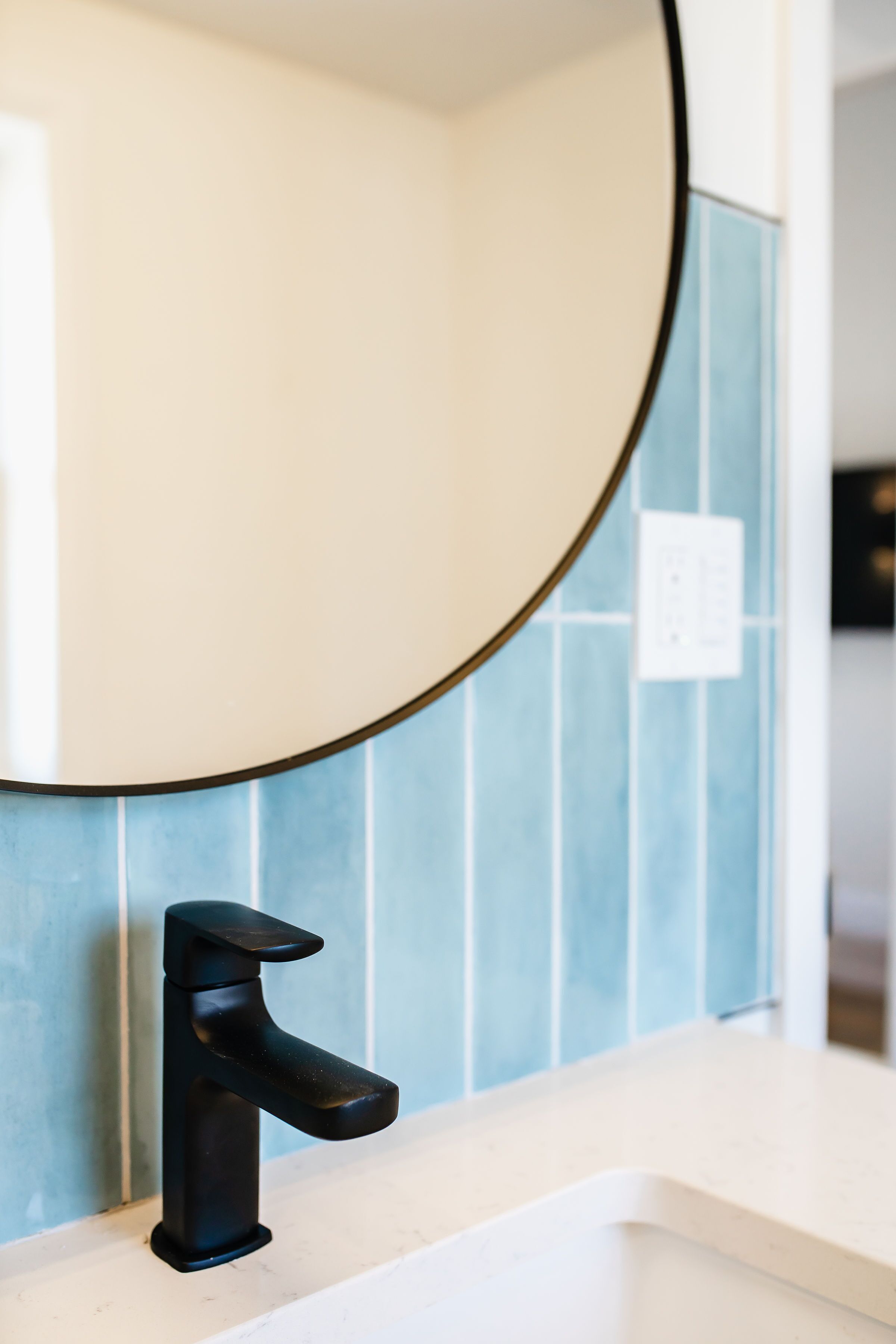 A bathroom with a black faucet, a round mirror, and blue tiled walls.