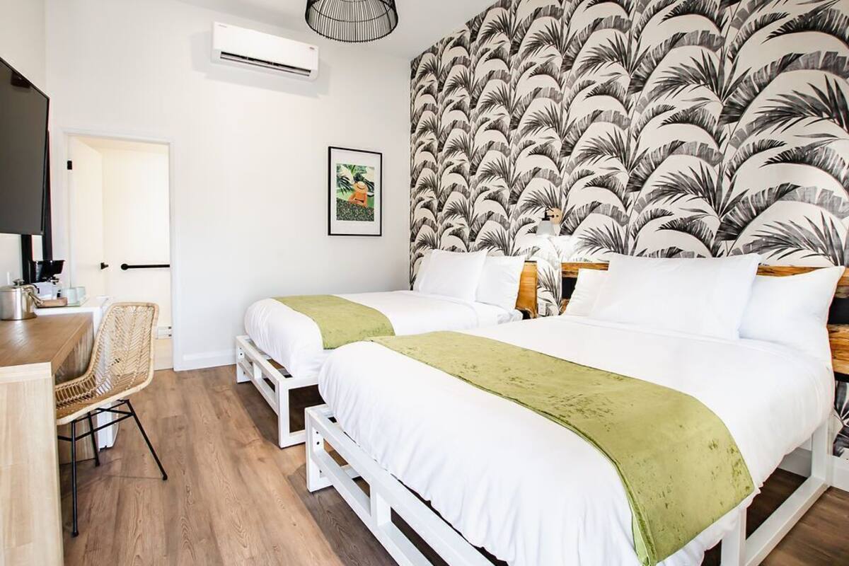 Een hotelkamer met twee bedden, een bureau, een stoel, een wandairconditioner en een lijst met een afbeelding.