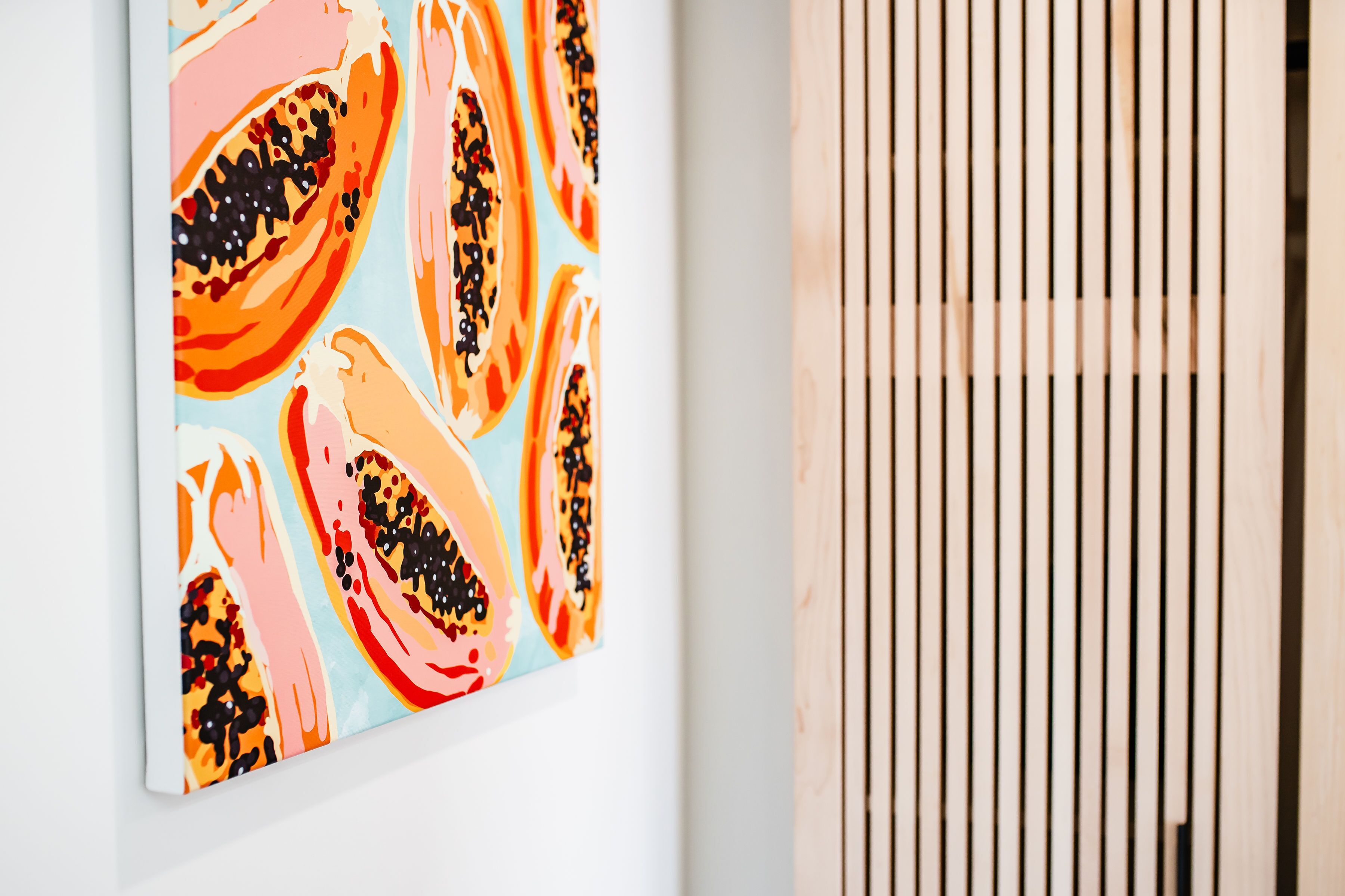 Una pared con una obra de arte vibrante de rodajas de papaya y un diseño de listones de madera verticales.