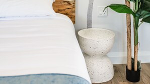 Une chambre avec un lit, une fresque murale représentant des palmiers, un luminaire suspendu et une plante en pot.
