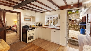 A kitchen with wooden beams, white cabinets, a stove, and a sink. - Southcott Farm Cottage (Honiton)