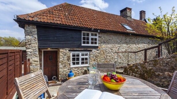 A stone house with a tiled roof, a wooden table with a bowl of fruit, and an open book. - Southcott Farm Cottage (Honiton)