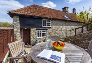 A stone house with a tiled roof, a wooden table with a bowl of fruit, and an open book. - Southcott Farm Cottage (Honiton)