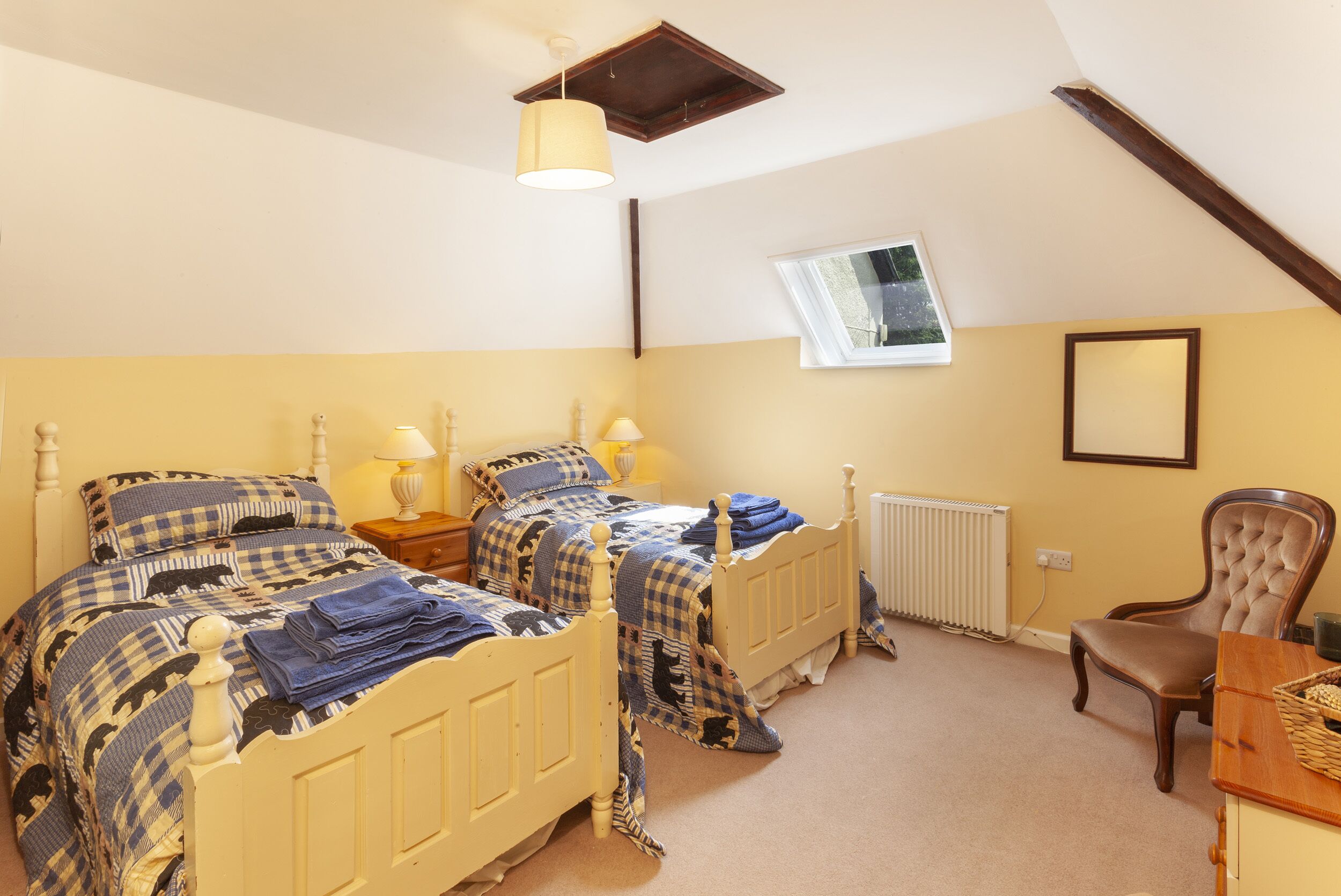 A bedroom with two beds, a wooden chair, a table, a window, and a radiator.
