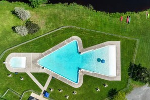 An aerial view of a swimming pool with a unique shape, surrounded by a well-maintained lawn and a few trees.