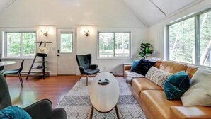 Ein geräumiges Wohnzimmer mit hohen Decken, großen Fenstern, einem Ledersofa, einem Couchtisch und einem Essbereich mit einem Stuhl und einem kleinen Tisch.
