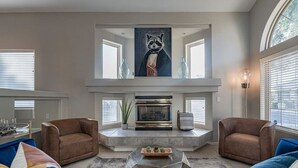 A living room with a fireplace, two armchairs, a sofa, and a large painting above the fireplace.